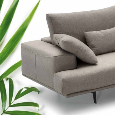 Sofá cinza claro com almofadas e pés pretos ao lado de folhas verdes