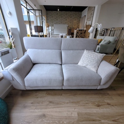 Sofá cinza claro com almofada branca numa sala de exposição de móveis