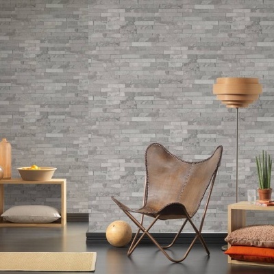 Cadeira de pele castanha com candeeiro e estantes de madeira clara contra parede cinzento tijolo