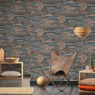 Sala com parede de tijolos cinza e castanhos, cadeira de pele castanha, mesa de madeira clara com vaso e candeeiro de pé de madeira.