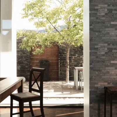 Sala de jantar com mesa em madeira escura, cadeira e parede em pedra cinzenta