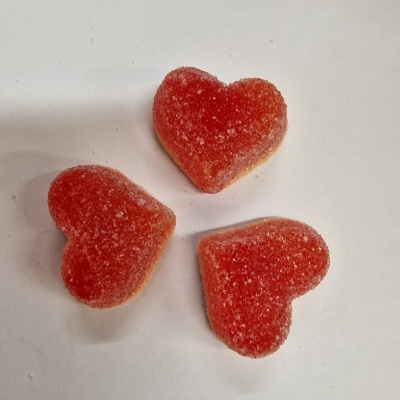 Três gomas vermelhas em forma de coração com açúcar em fundo branco