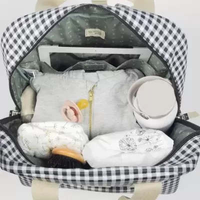 Mochila xadrez aberta com casaco cinza, chupeta, garrafa, escova, fralda e objeto com desenho floral
