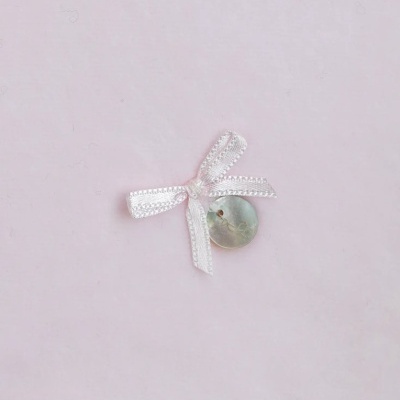 Botão madre-pérola com laço rosa claro sobre fundo rosa pálido