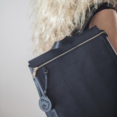 Mala preta com fecho zip dourado e pendente redondo preto usada por mulher de cabelos cacheados