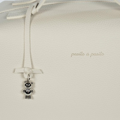 Parte de saco de pele branca com pendente em forma de ursinho e texto 'pasito a pasito'