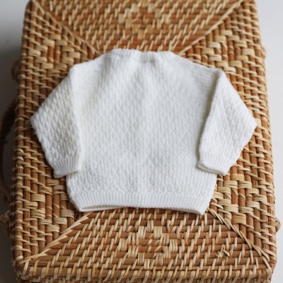 Camisa de malha branca para bebé sobre caixa de vime trançado