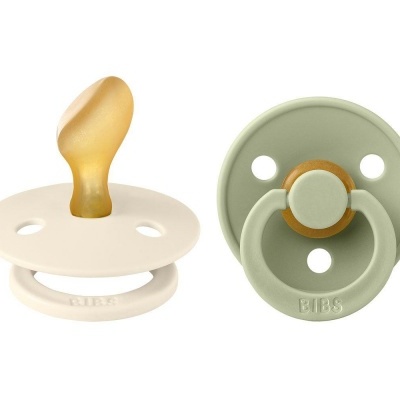 Duas chupetas BIBS, uma bege com bico amarelado e outra verde com argola, ambas redondas