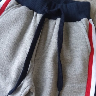 Calças de treino cinzentas com faixas laterais coloridas sobre chão de madeira