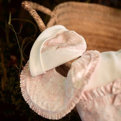 Conjunto de babygrow e gorro branco com padrão floral cor-de-rosa em cesta de vime.