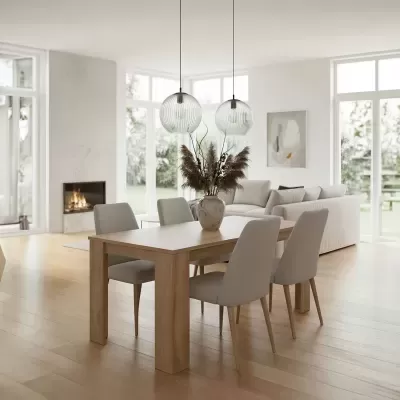 Mesa de jantar de madeira clara com quatro cadeiras estofadas cinza claro e candeeiros pendentes em vidro transparente