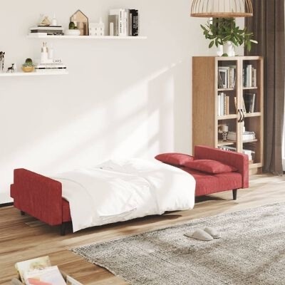 Sofá-cama vermelho aberto com manta branca em sala com estante de madeira e cortinas castanhas