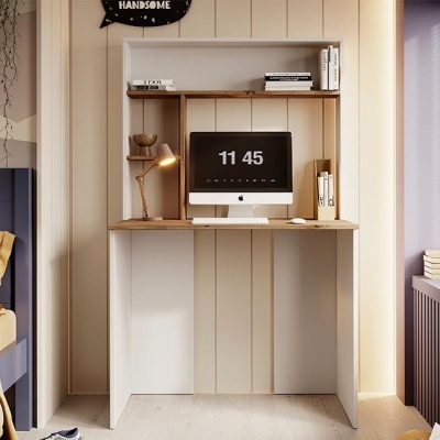 Secretária de madeira clara com computador Apple e candeeiro, prateleira com livros, num quarto claro