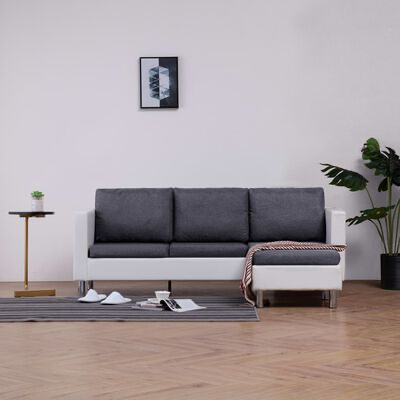 Sofá cinzento e branco com chaise longue, manta, tapete riscado, mesa lateral dourada, planta e quadro abstrato num interior.