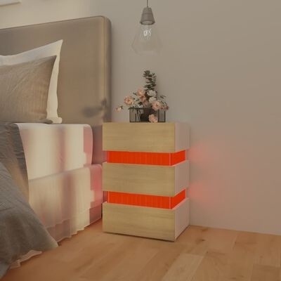 Mesa de cabeceira em madeira clara com faixas vermelhas iluminadas ao lado de cama com cabeceira cinza e roupa de cama cinza