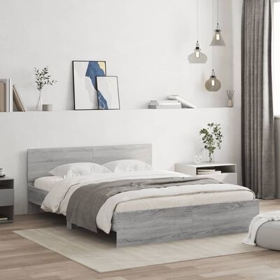 Quarto minimalista com cama de madeira cinzenta, roupa branca e manta cinza, mesinhas com plantas, candeeiros suspensos e pinturas na parede
