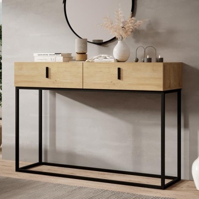 Cómoda de madeira clara com estrutura preta, vasos, velas e livros em cima, parede cinza e espelho redondo ao fundo