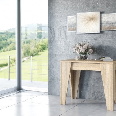 Mesa de madeira clara com decoração numa sala com parede cinzenta e janelas grandes para paisagem verde