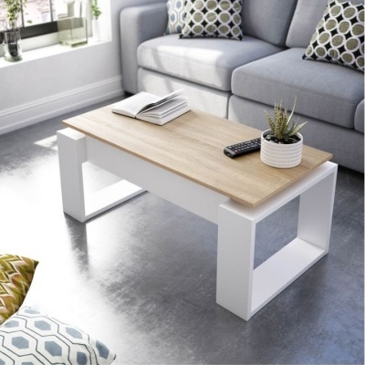 Mesa de centro com tampo de madeira clara e base branca, com livro, comando e vaso com planta, ao fundo sofá cinzento com almofadas geométricas