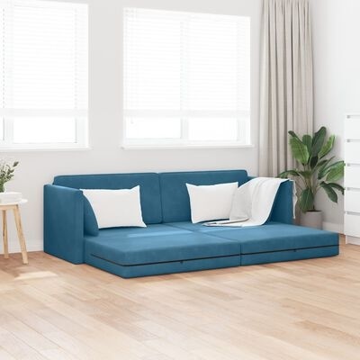 Sofa azul com almofadas brancas e manta numa sala com chão de madeira e planta verde