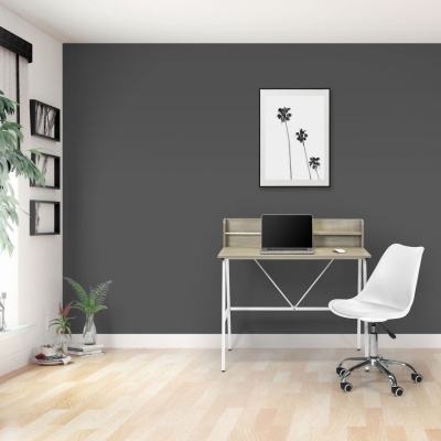 Escrivaninha de madeira clara com cadeira branca e fundo de parede cinza escuro com quadro de flores pretas