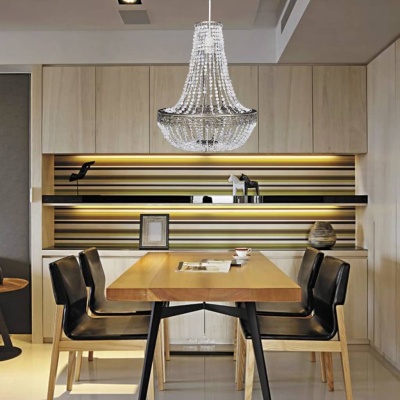 Sala de jantar com mesa de madeira clara, cadeiras pretas com pernas de madeira clara e candeeiro de teto de cristal