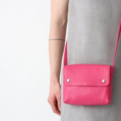 Bolsa rosa fúcsia pequena com aba e botões prateados usada ao ombro