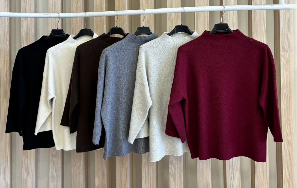 Camisolas de vários tons de malha penduradas em cabides numa barra branca