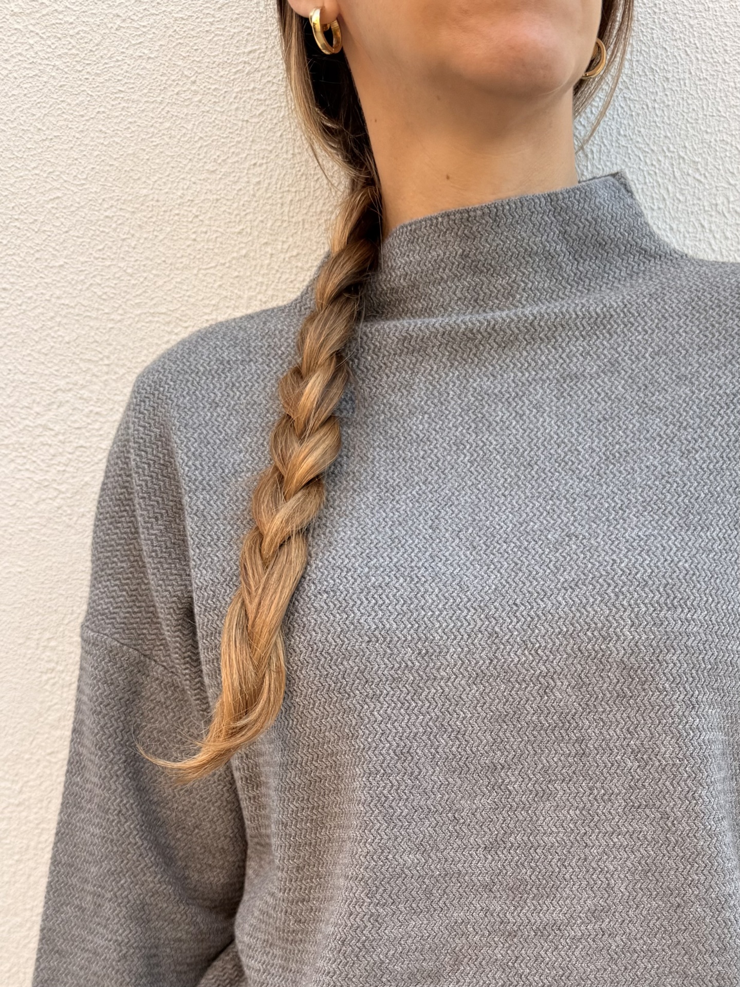 Camisola cinzenta de malha com padrão zigzag e gola alta, cabelo trançado e brincos dourados.