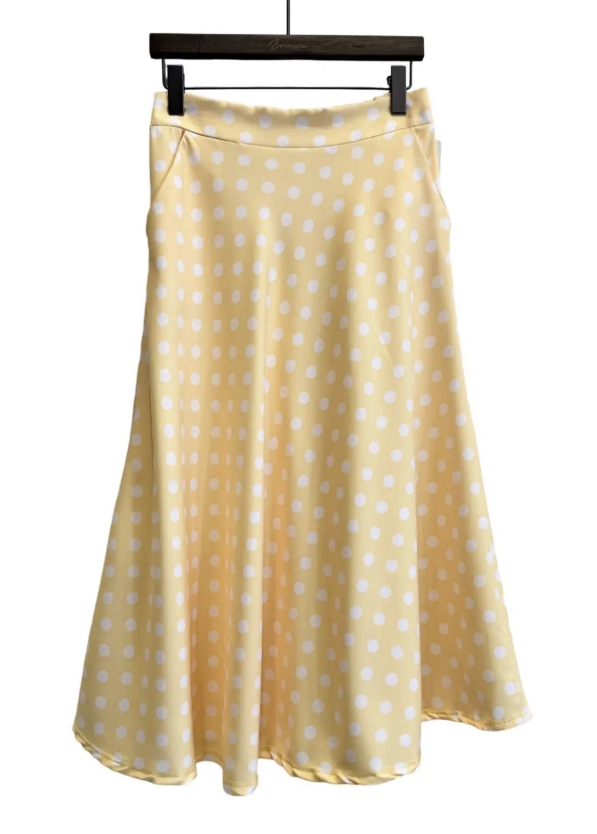 Saia amarela clara com bolas brancas pendurada em cabide de madeira
