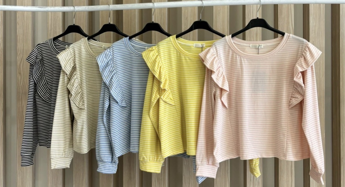 Cinco blusas às riscas com volantes nas mangas, em várias cores, penduradas em cabides pretos