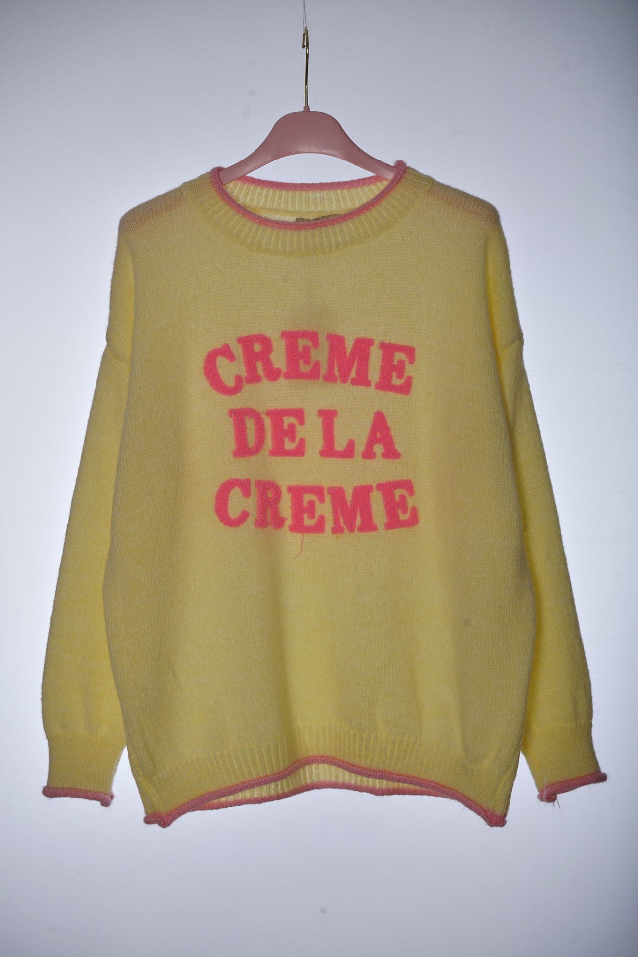 camisola amarela com texto rosa CREME DE LA CREME pendurada num cabide rosa