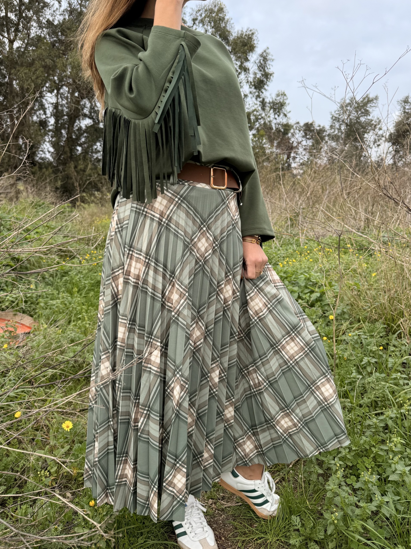 saia plissada xadrez verde bege castanho, camisola verde com franjas, cinto castanho, sapatilhas brancas riscas verdes em campo