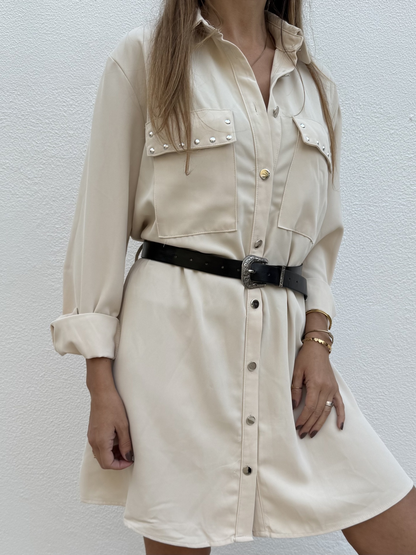 Vestido camisa bege com botões e bolsos com tachas, cinto preto com fivela, manga arregaçada