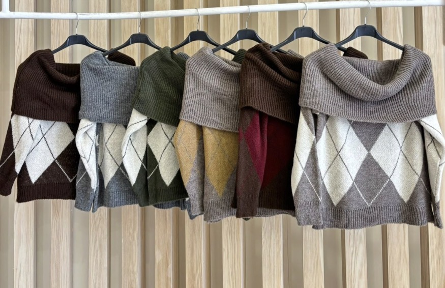 Seis camisolas de malha com padrão em losangos em várias cores penduradas em cabides