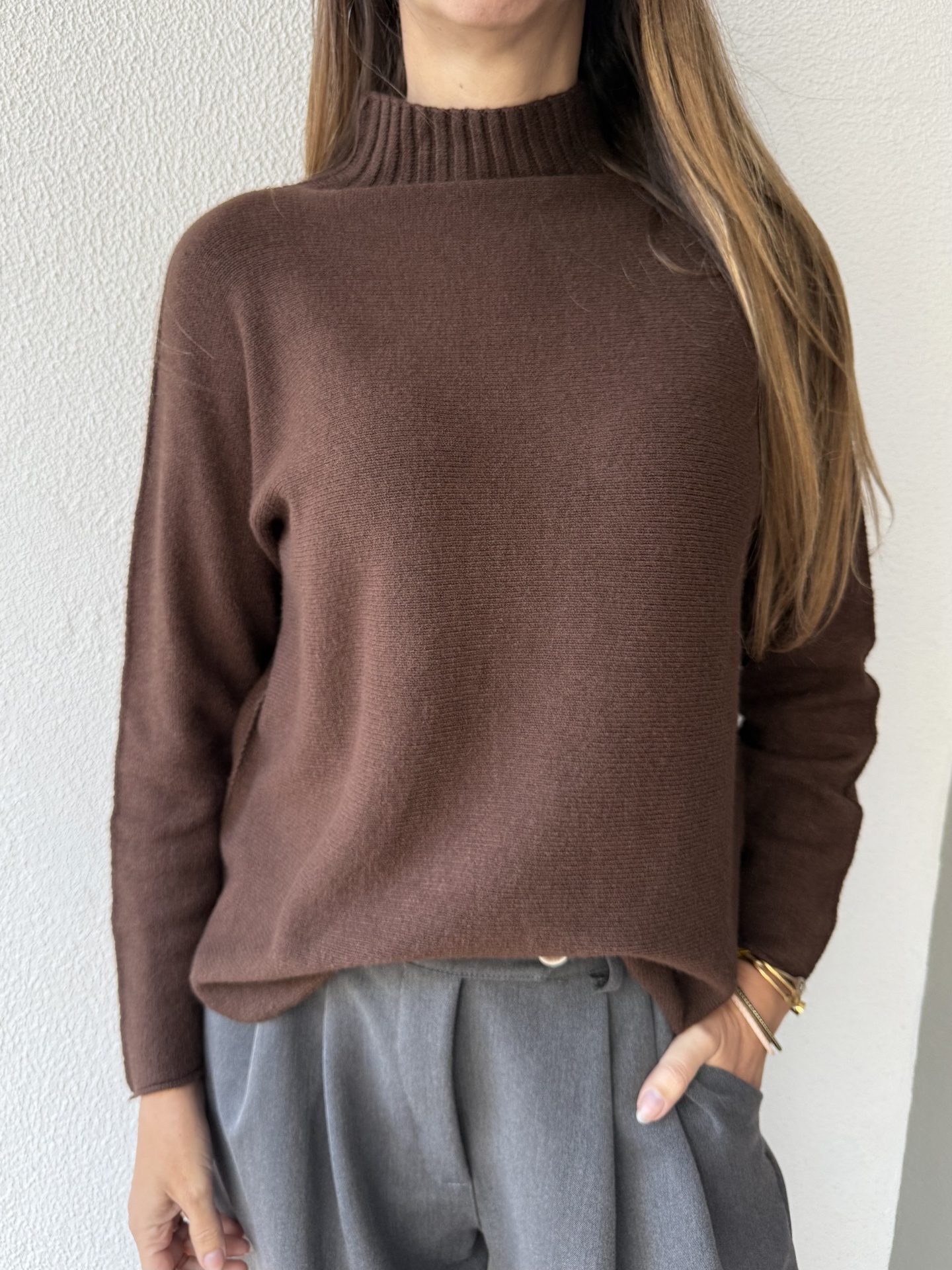 Suéter castanho de gola alta e calças cinza numa pessoa, fundo branco