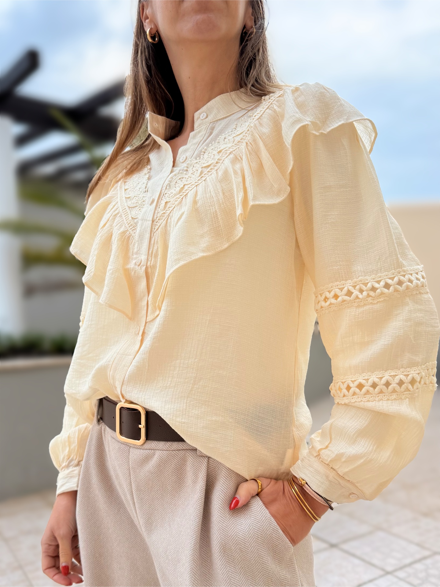 Blusa feminina creme com babados e renda nas mangas, combinada com calças claras e cinto preto