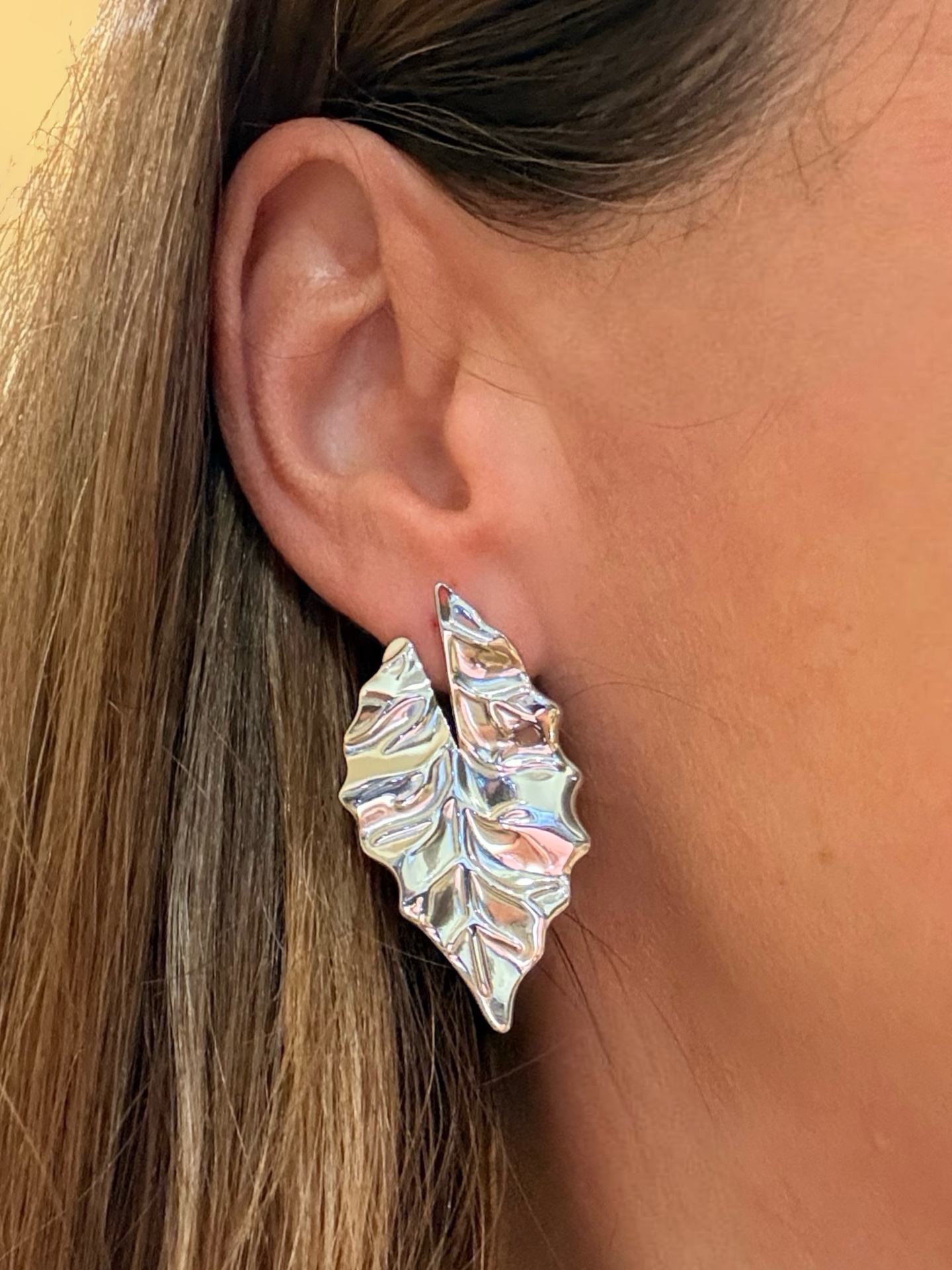 Brinco prateado em forma de folha na orelha de uma pessoa