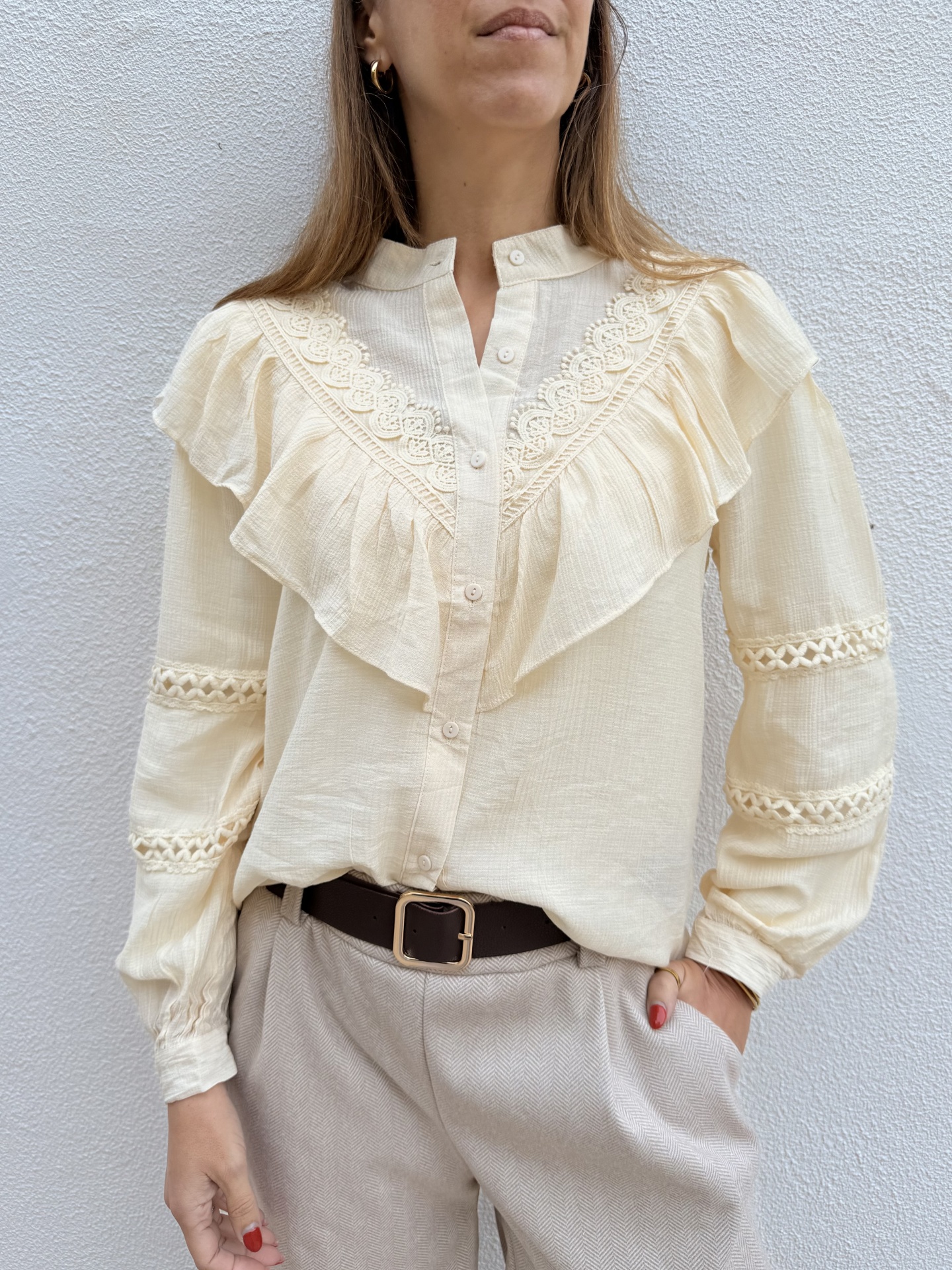 Camisa creme com folhos e rendas, calças bege e cinto castanho com fivela dourada