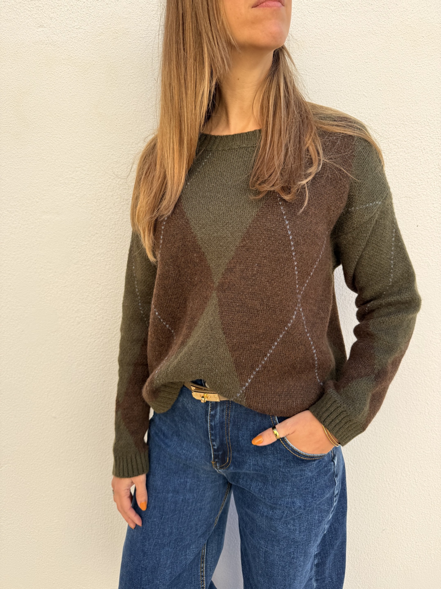 Camisola de malha verde e castanha com padrão de losangos e calças de ganga azuis