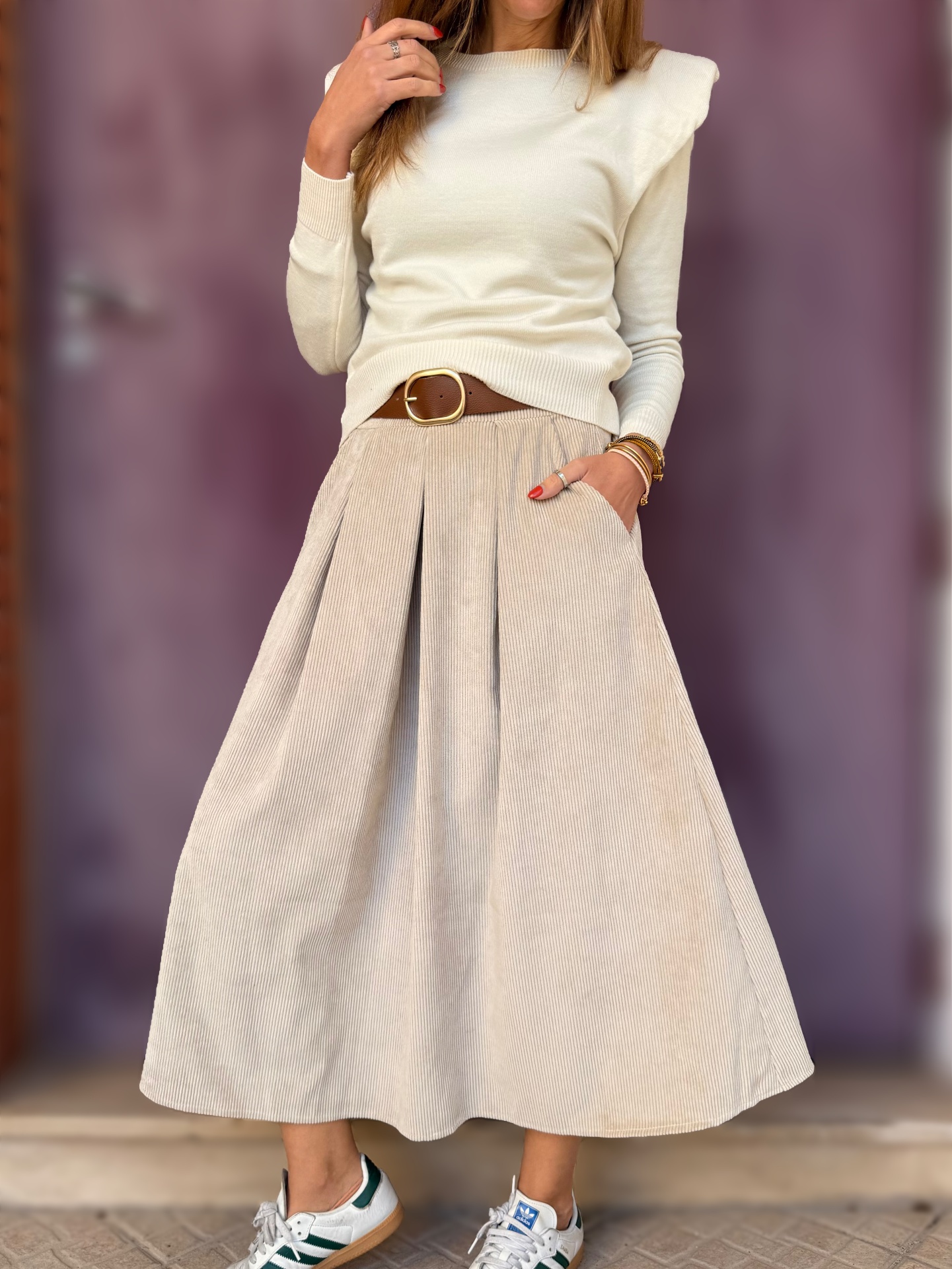 Vestuário feminino com vestido midi bege, cinto castanho, camisola creme e ténis brancos verdes