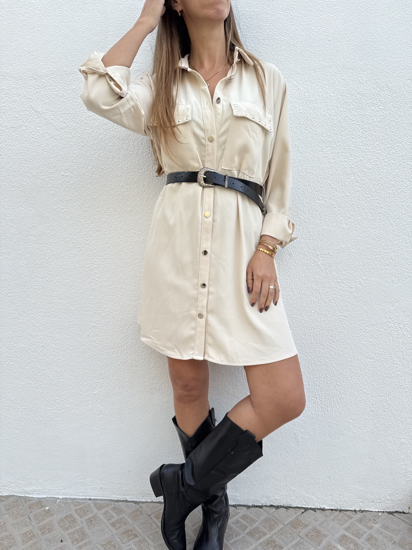 Vestido camisa creme com cinto preto e botas pretas em parede branca