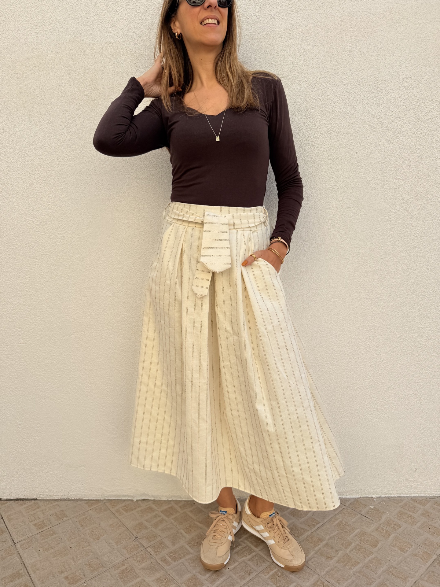 Saia longa creme riscada com t-shirt castanha e ténis bege num chão de azulejo