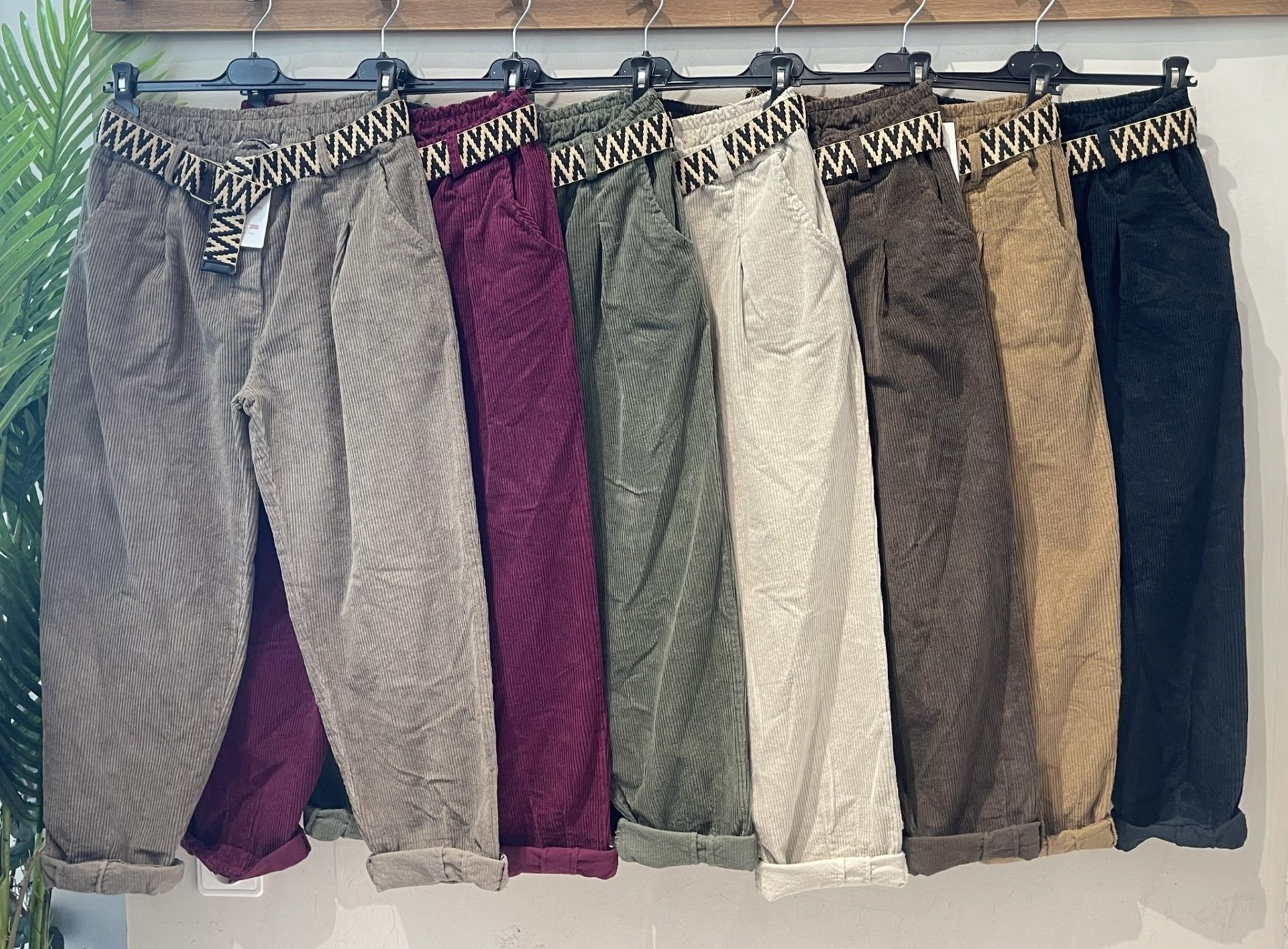 Sete calças de veludo cotelê em várias cores com cintos tecido e padrão geométrico penduradas numa barra de madeira