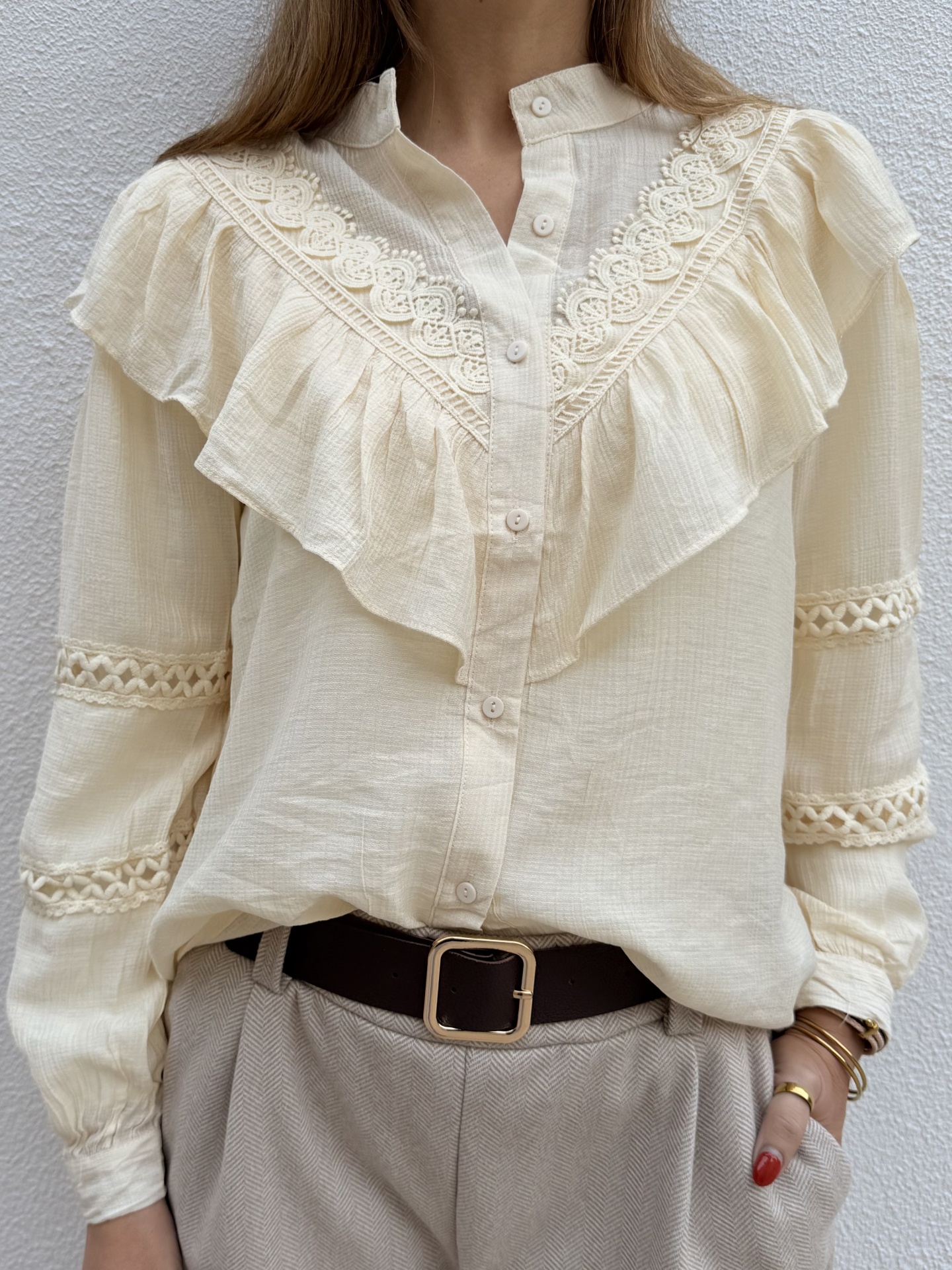 Blusa creme com folhos e renda, cinto castanho e calças bege com padrão espinha de peixe