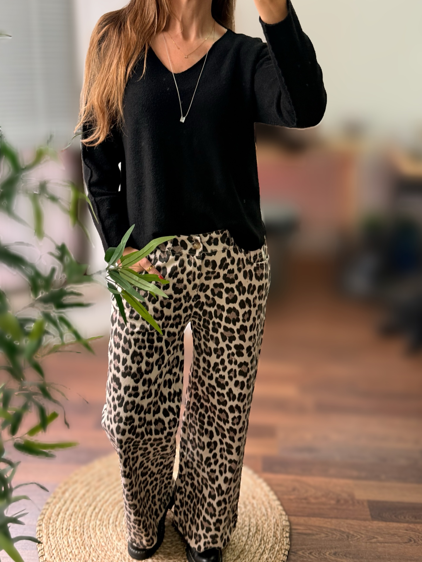 Pessoa vestindo camisola preta de manga longa e calças com padrão animal print num ambiente interior