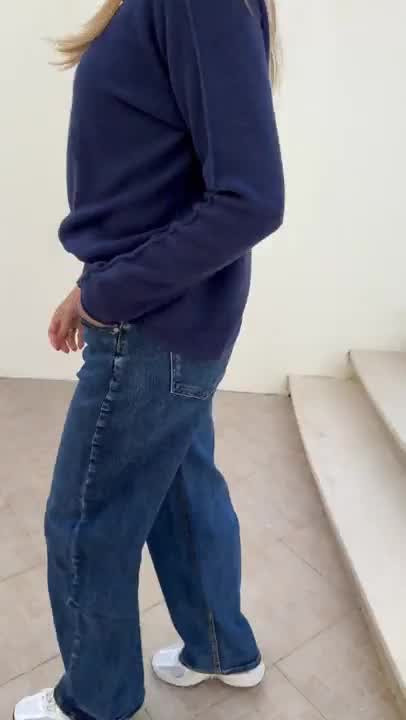 Pessoa de jeans azuis e camisola azul escura em espaço interior com escada de betão