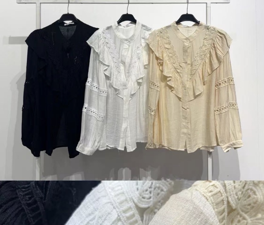 Três blusas femininas de manga longa com renda e folhos em preto, branco e bege penduradas.