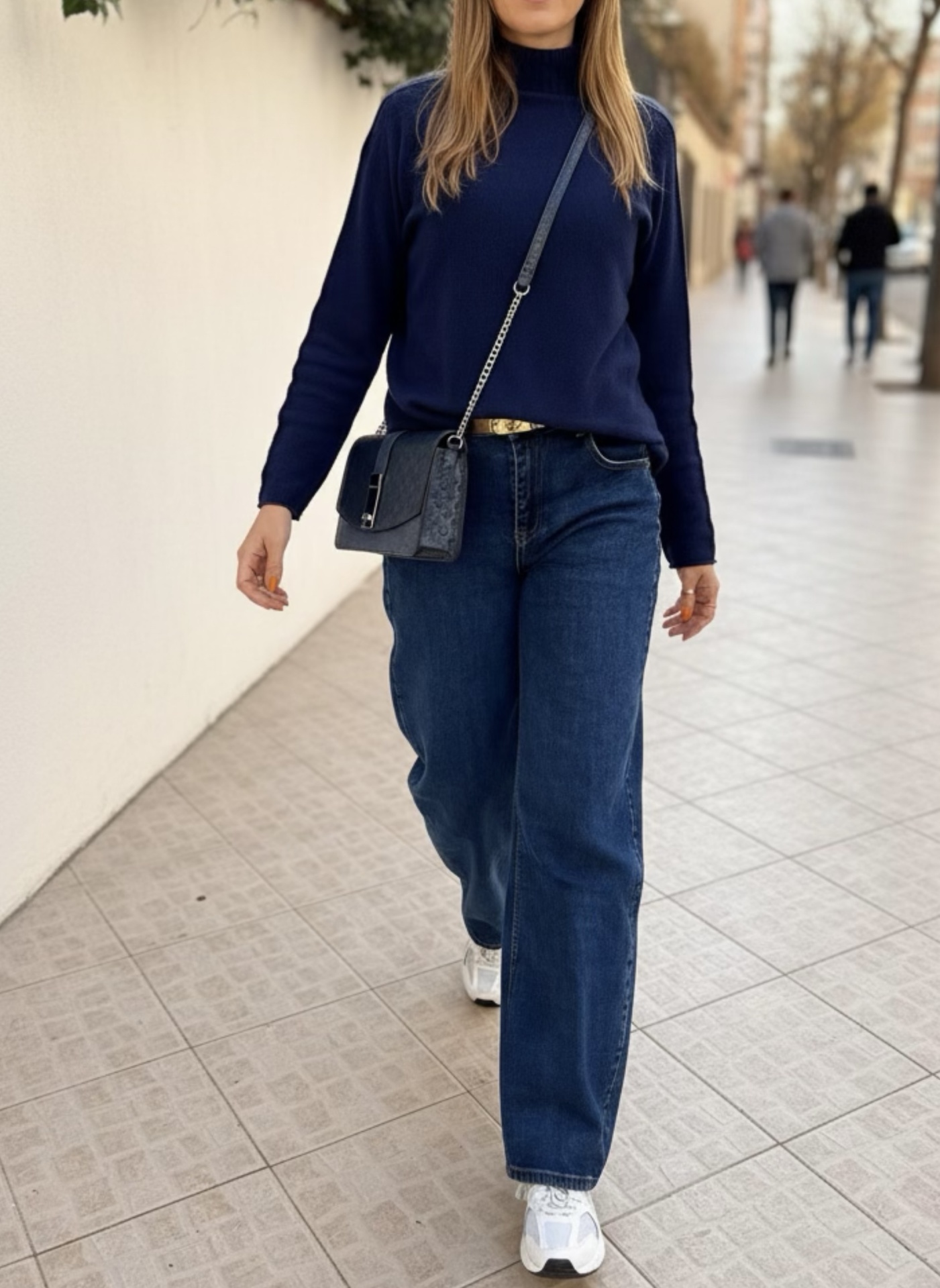 Mulher com camisola azul, calças de ganga largas e mala preta a caminhar na rua