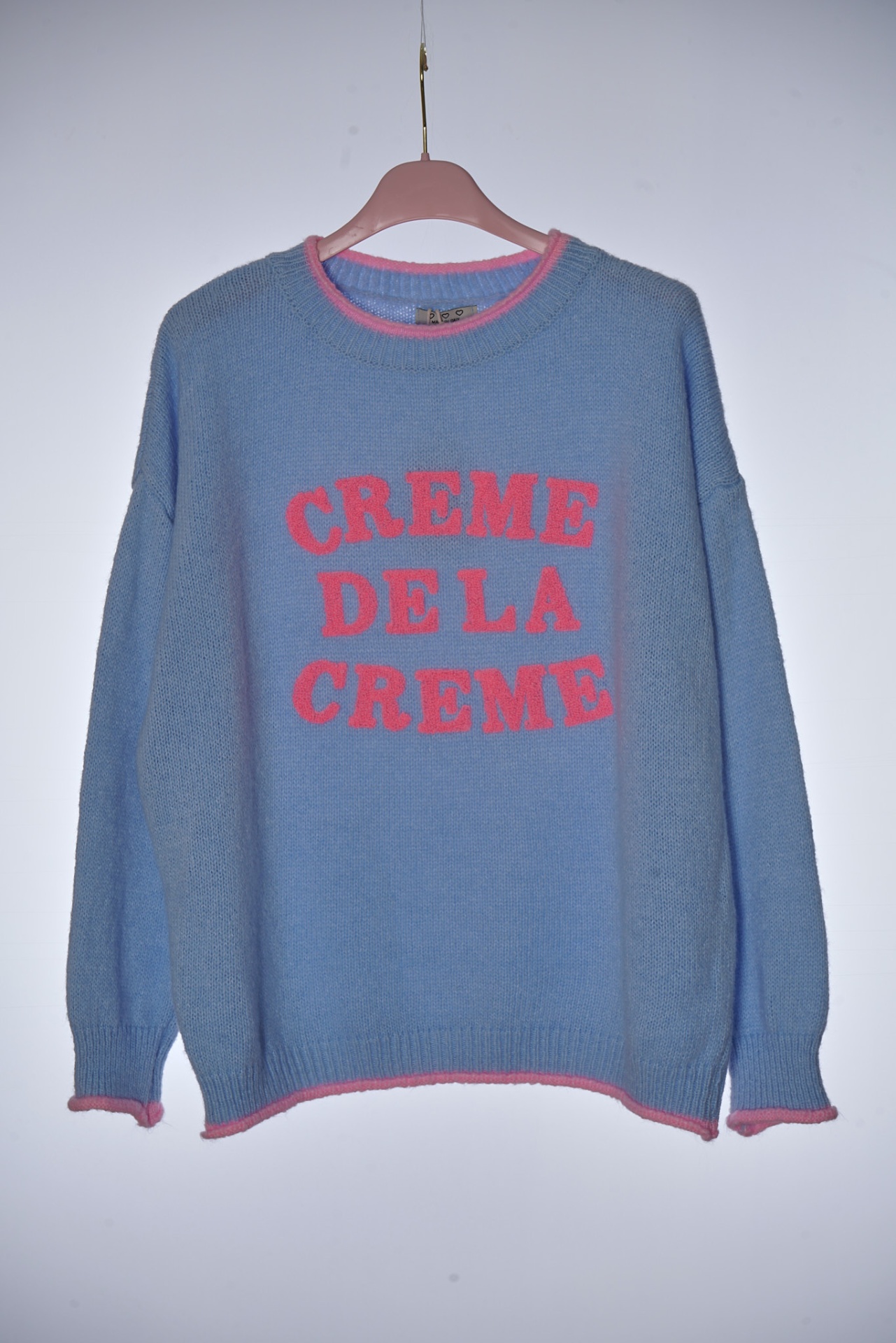 Camisola azul com texto rosa CREME DE LA CREME em cabide rosa